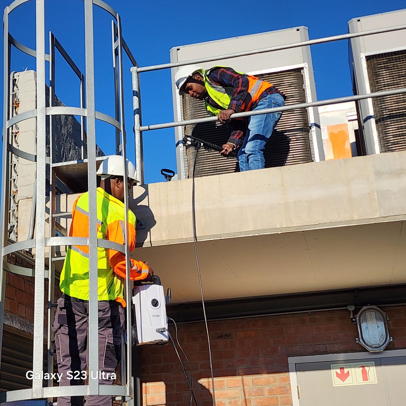 Two technicians working from an access ladder on site