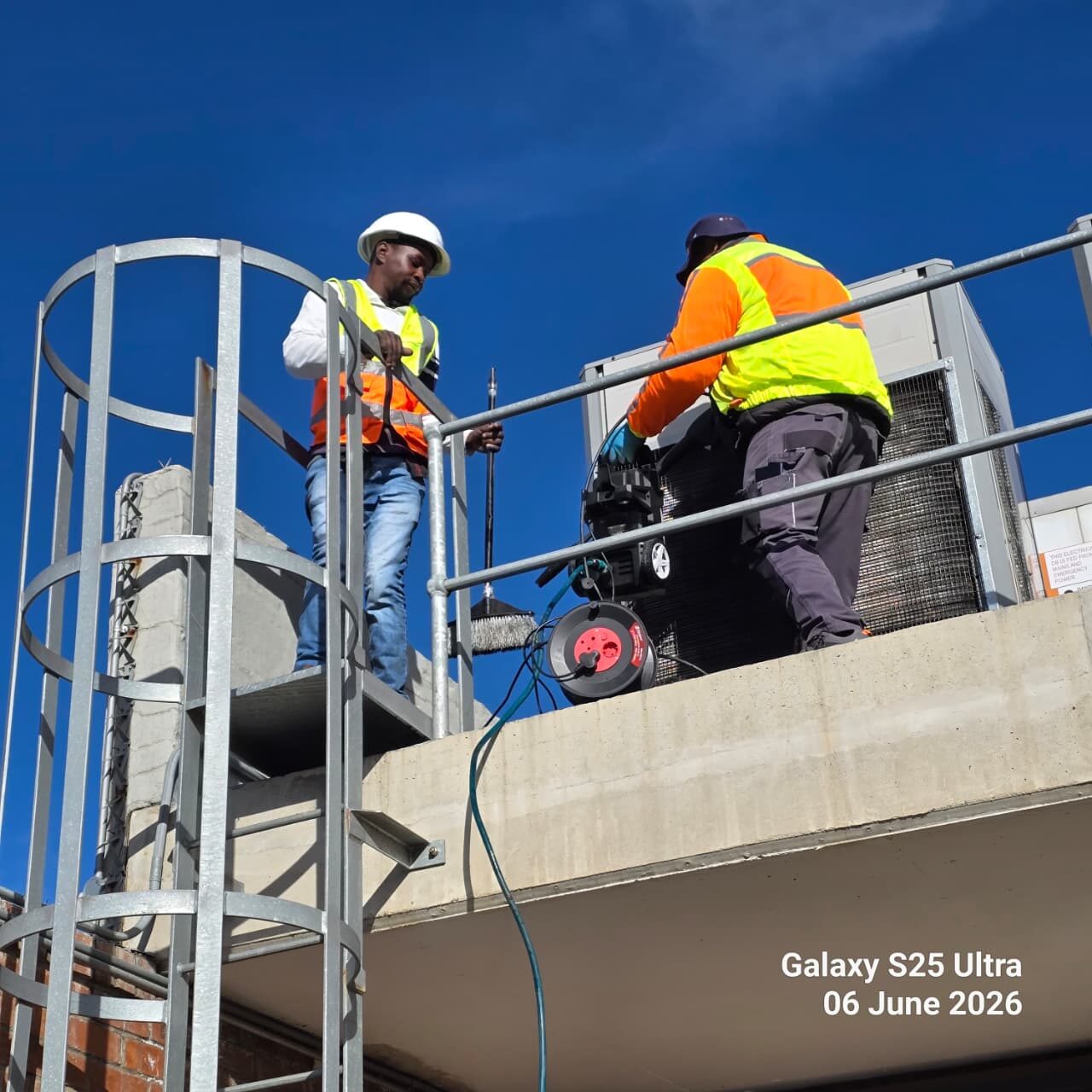 Two technicians servicing rooftop HVAC plant against a clear sky